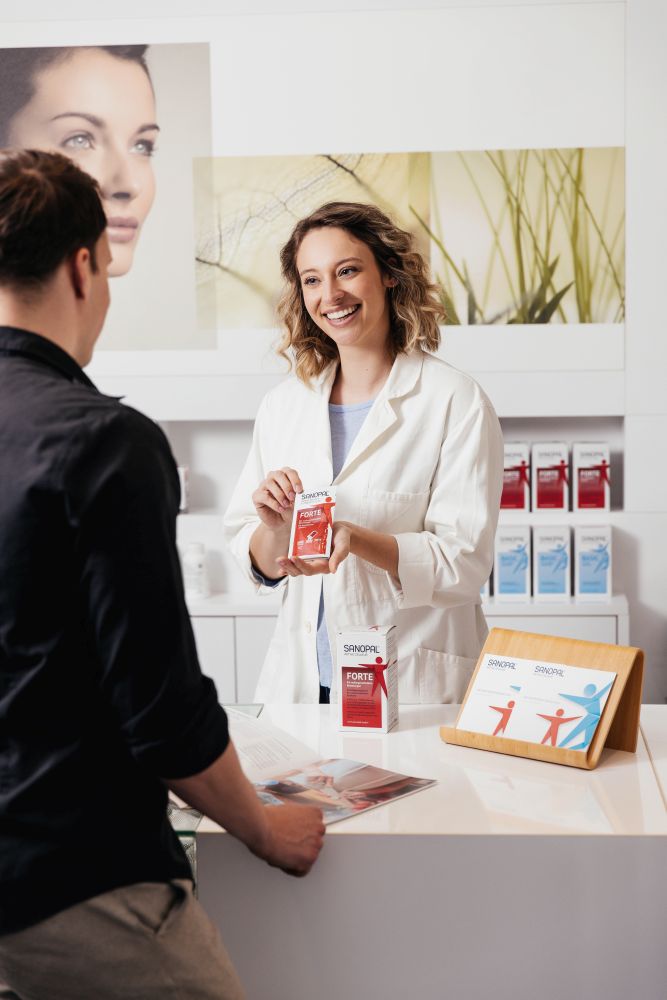 Apothekerin empfiehlt Sanopal Forte einem Kunden an der Apothekentheke – kompetente Beratung zur Aktiven Zellkur bei RDNS, Burnout und posttraumatischem Stress in der Apotheke