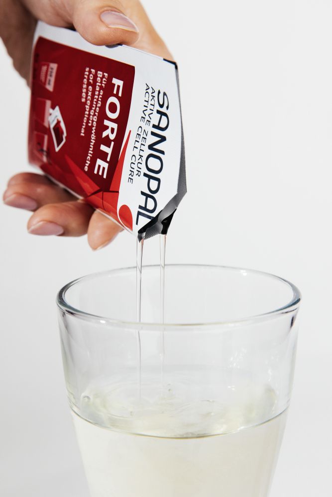 Hand gießt Sanopal Forte Sachet in ein Glas mit Wasser – einfache tägliche Einnahme der Aktiven Zellkur bei außergewöhnlichen Belastungen wie Burnout, Long COVID und posttraumatischem Stress